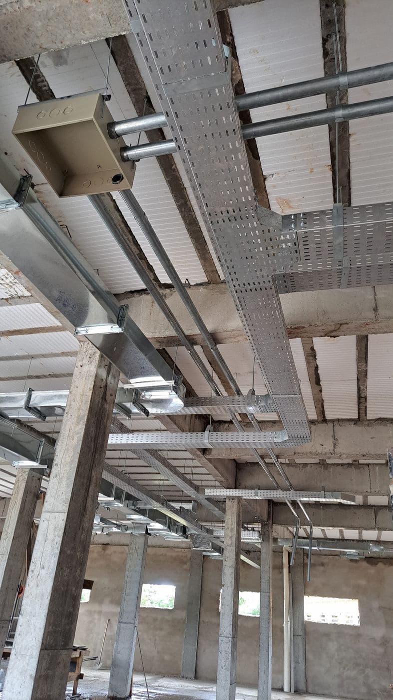 Infraestrutura em eletrocalha: Eletrocalhas perfuradas e eletrodutos aparentes distribuindo os circuitos de um galpão.