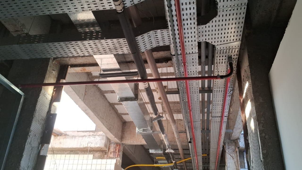 Infraestrutura aparente: Eletrocalhas e eletrodutos aparentes passando pela laje de uma obra comercial.