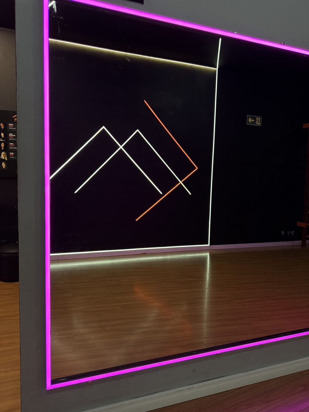 Academia, sala de aula: Moldura de LED rosa no espelho e logotipo desenhado com perfis de LED na parede.
