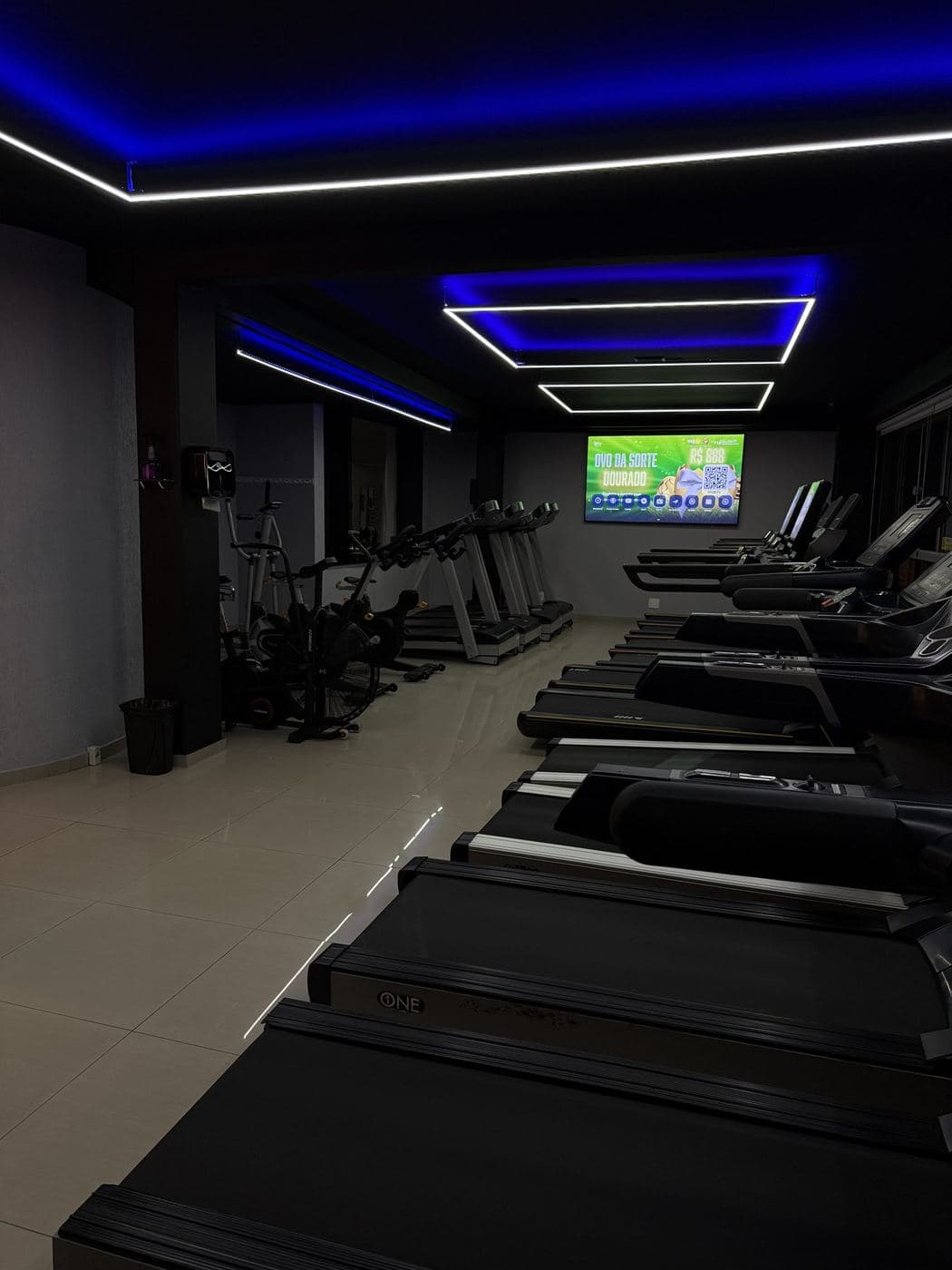 Academia, esteiras: Quadros de LED em sequência no teto, acompanhando as fileiras de esteiras.