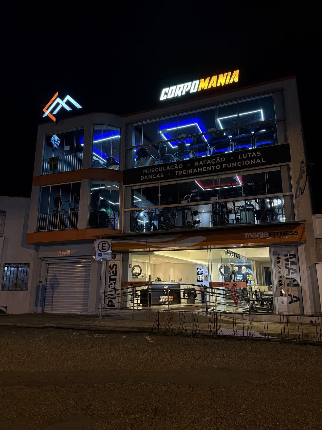 Fachada de academia: Fachada de três andares com letreiro e logotipo iluminados e os quadros de LED visíveis pelos vidros.
