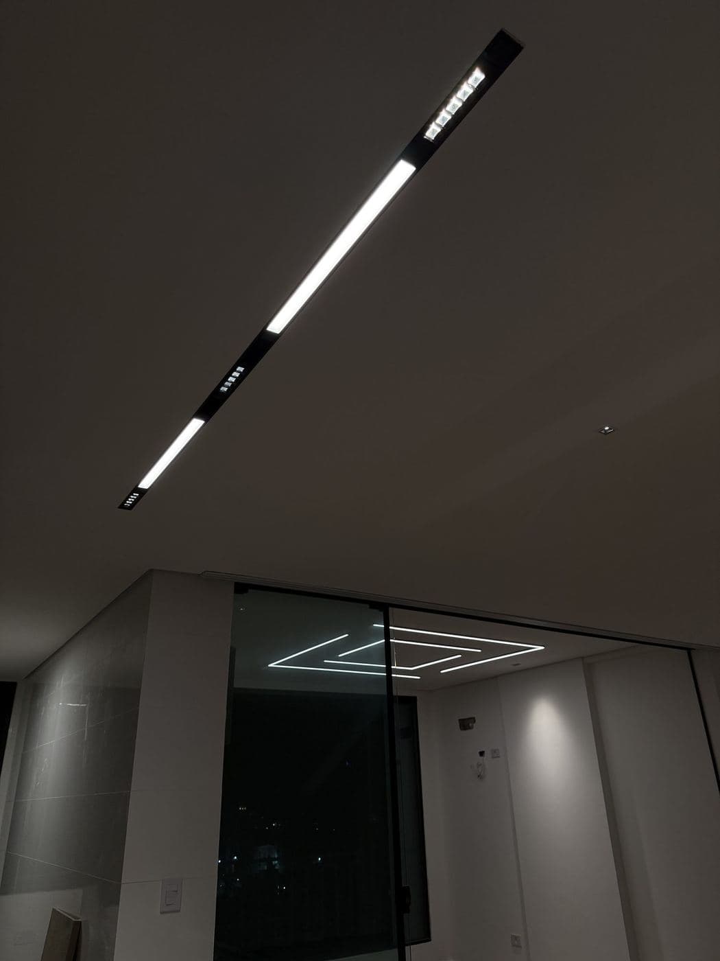Luminária linear: Luminária linear de LED embutida no forro, alinhada com a iluminação do ambiente vizinho.