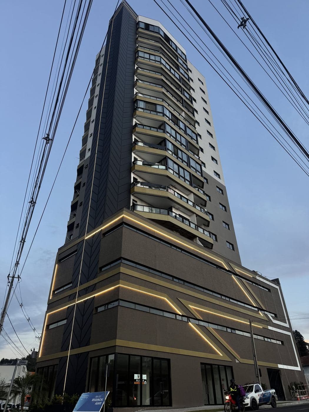Base de edifício: Perfis de LED dourados em linhas e diagonais desenhando a base do prédio.