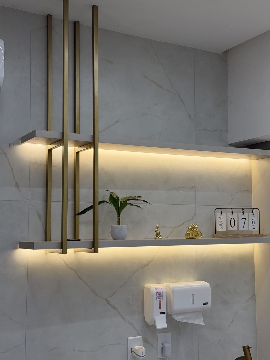 Lavabo com prateleiras iluminadas: Fita de LED sob as prateleiras, com luz quente sobre a parede de mármore.