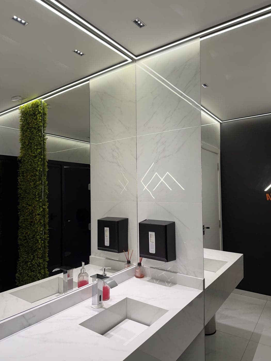 Lavatório de academia: Perfil de LED no forro, logotipo na parede e luz de destaque no jardim vertical.