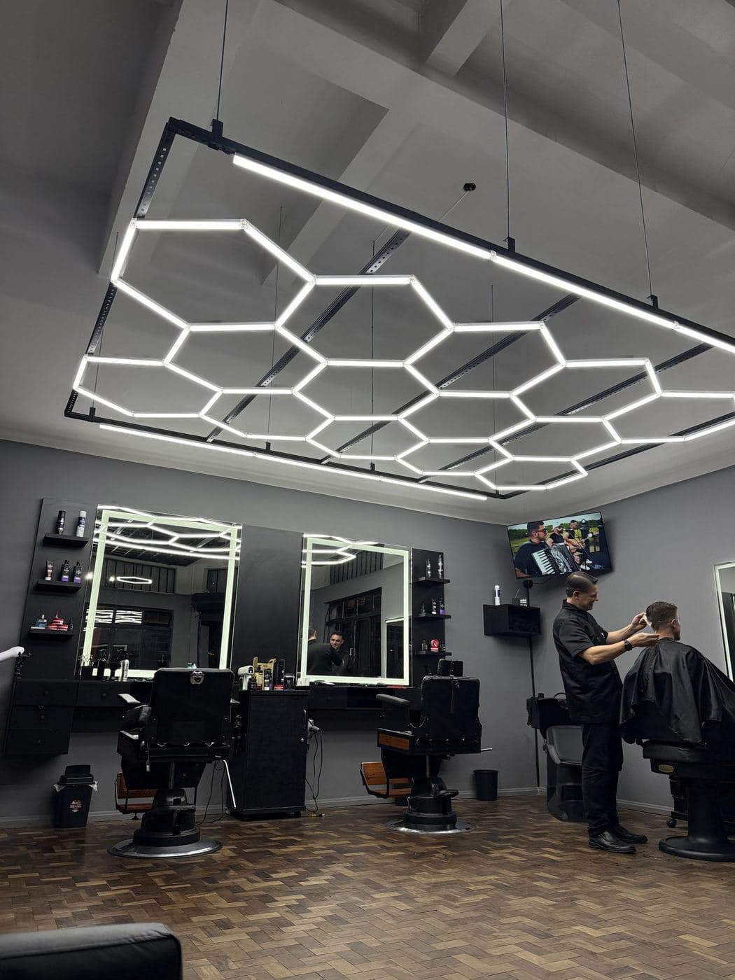 Barbearia: Luminária hexagonal de LED sobre as cadeiras e espelhos com moldura de luz.