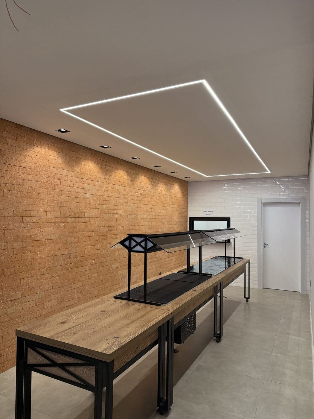 Espaço de buffet: Retângulo de perfil de LED no forro e spots direcionados para a parede de tijolos.