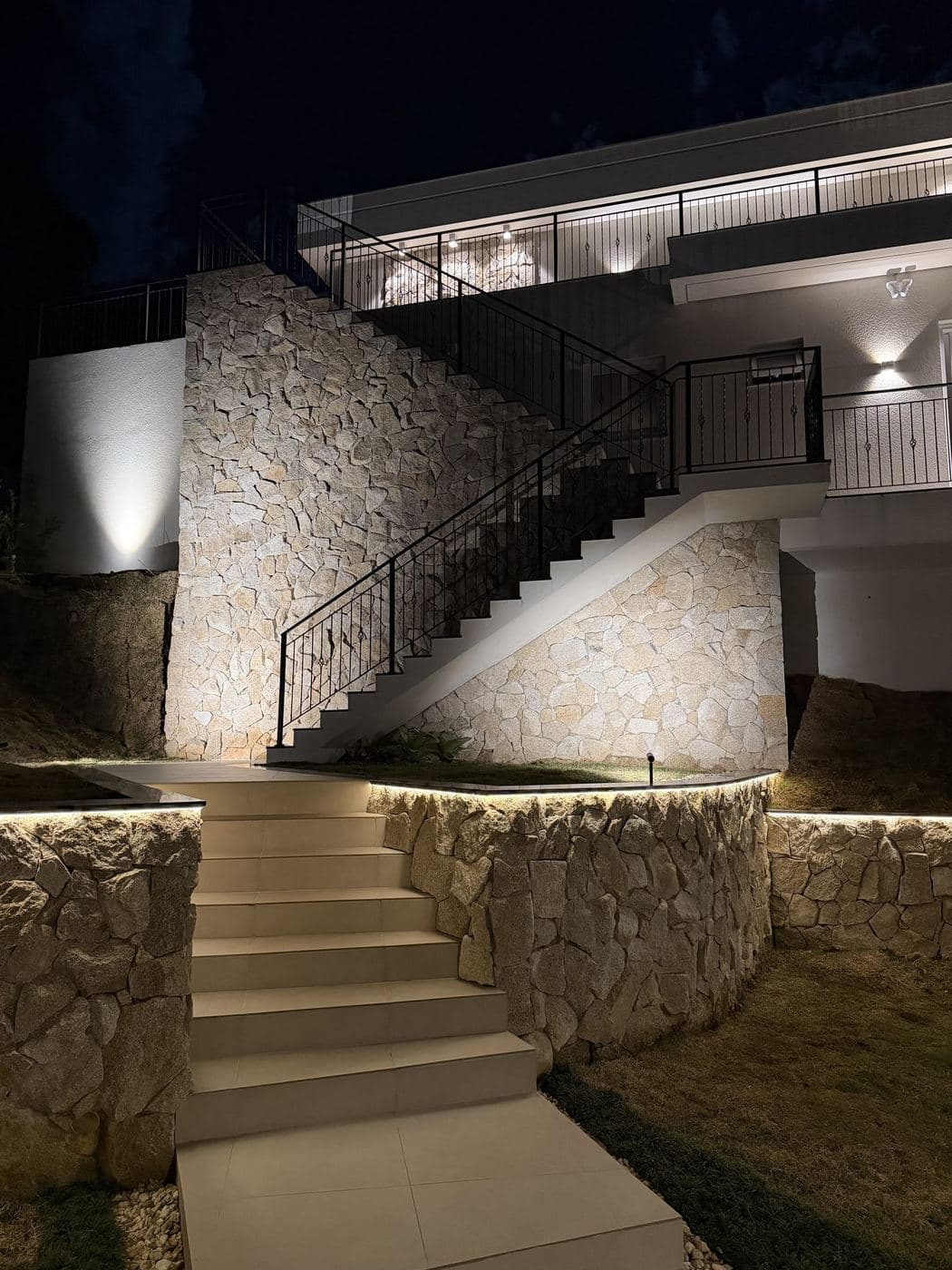 Escada e muros de pedra: Luz de destaque nos muros de pedra, fita de LED na base das floreiras e arandelas na área de lazer.